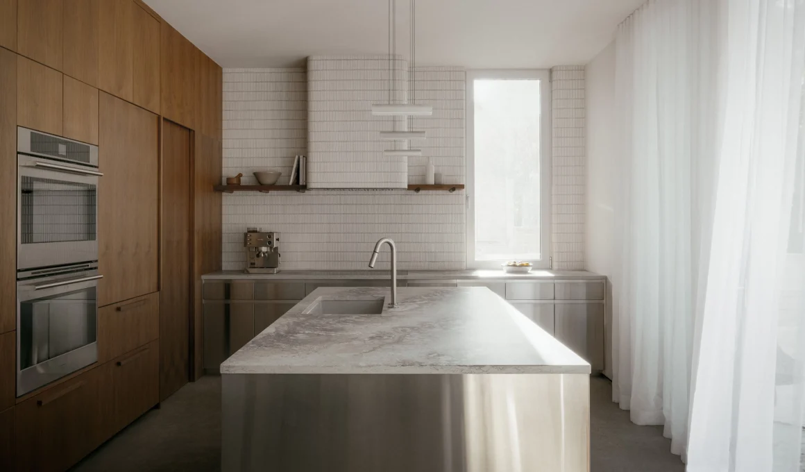 Luxury residential kitchen design featuring stainless steel cabinets, polished concrete floor, and warm walnut accents. Project L'Ecrin Residence by Appareil Architecture.