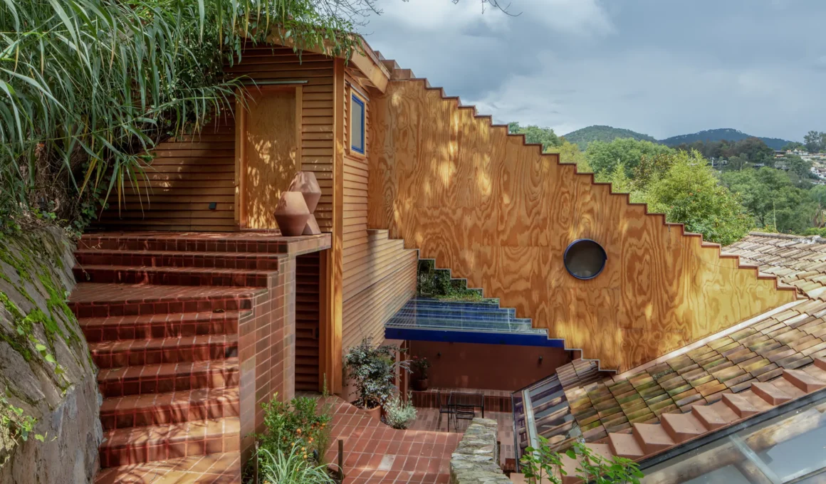 Pedro & Juana Wooden Annex Valle de Bravo. View showing the timber extension, new roof-piercing staircase tunnel, and brick patio on the sloping mountainside.