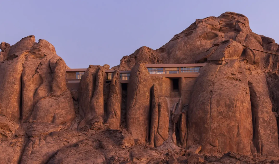 The Desert Rock resort in Saudi Arabia by Oppenheim Architecture, showing guest suites excavated directly into the ancient granite mountains to achieve a seamless blend of luxury hospitality and the natural wilderness.