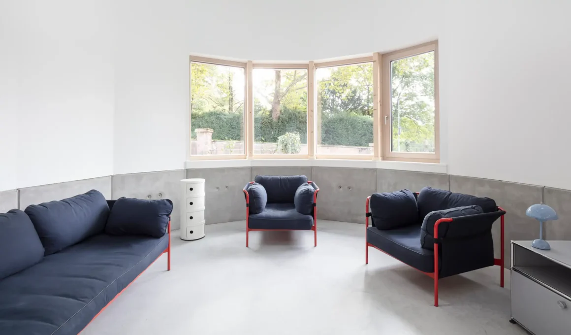 Curved modern living room interior of House HSBW in Heidelberg, Germany, designed by Simon Kochhan, showcasing the unique site-specific geometry, large windows, and polished screed floor for contemporary urban living.