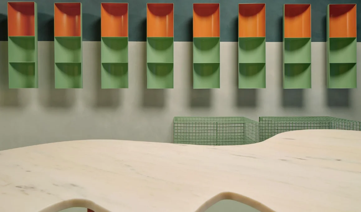 Interior view of Laconicum store Madrid showing curved custom green shelving system, pink Estremoz marble Río table, and vertical lighting by Lucas y Hernández-Gil.