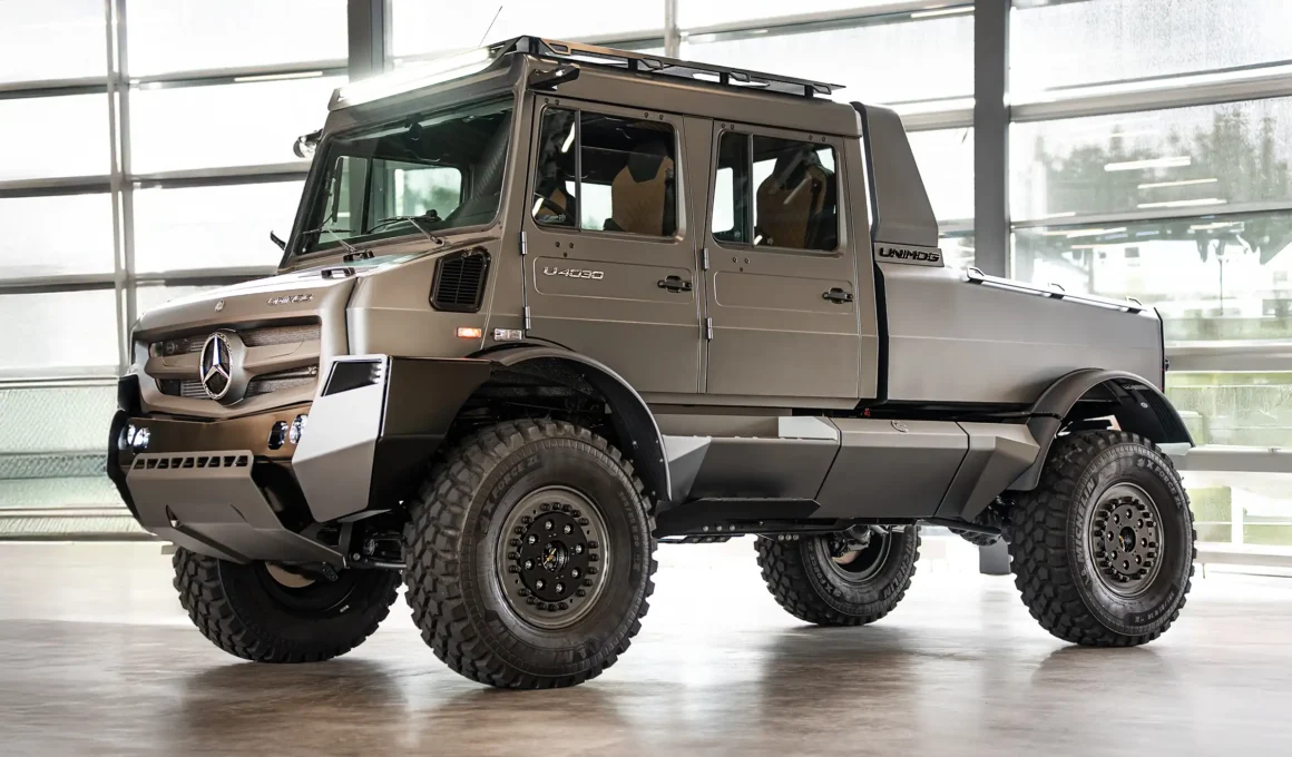 A high-angle front view of the new Mercedes-Benz luxury Unimog show car featuring matte grey paint, massive off-road tires, and a double cab interior in a professional showroom setting.