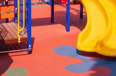 Modern playground safety surfacing with yellow slide and colorful, inclusive play equipment for children.