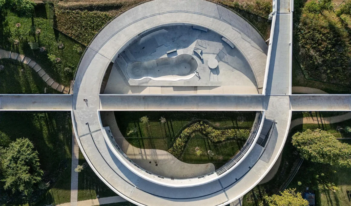 Aerial perspective of the Petit-Quevilly redevelopment site featuring a large circular walkway and a metropolitan footbridge designed by Olgga Architectes to connect the sports complex with the surrounding city.