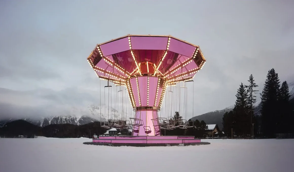 A vibrant pink mirrored carousel installation by Carsten Höller situated on a vast snow-covered ice rink in St. Moritz, set against a backdrop of fog-shrouded alpine mountains at dusk.