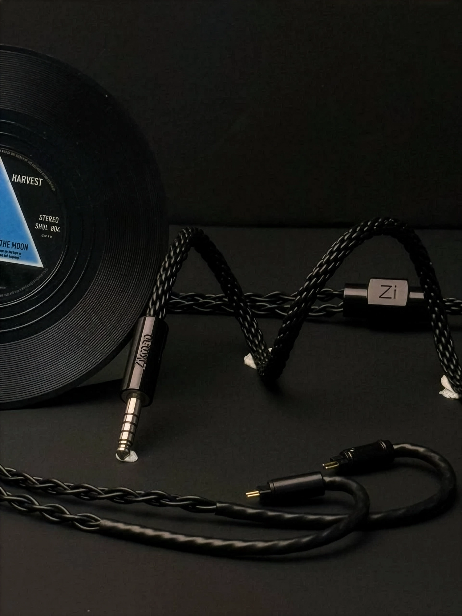 Black braided 2-pin IEM cable by Zikman audio with matte metal hardware, displayed next to a vinyl record.
