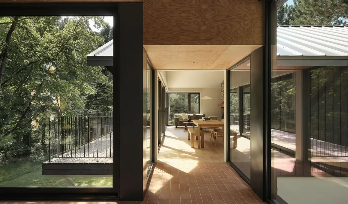 Interior view of the Saint-Ferréol Résidence showing an aerial walkway with terracotta flooring and glass walls connecting a modern timber pavilion to the original home.