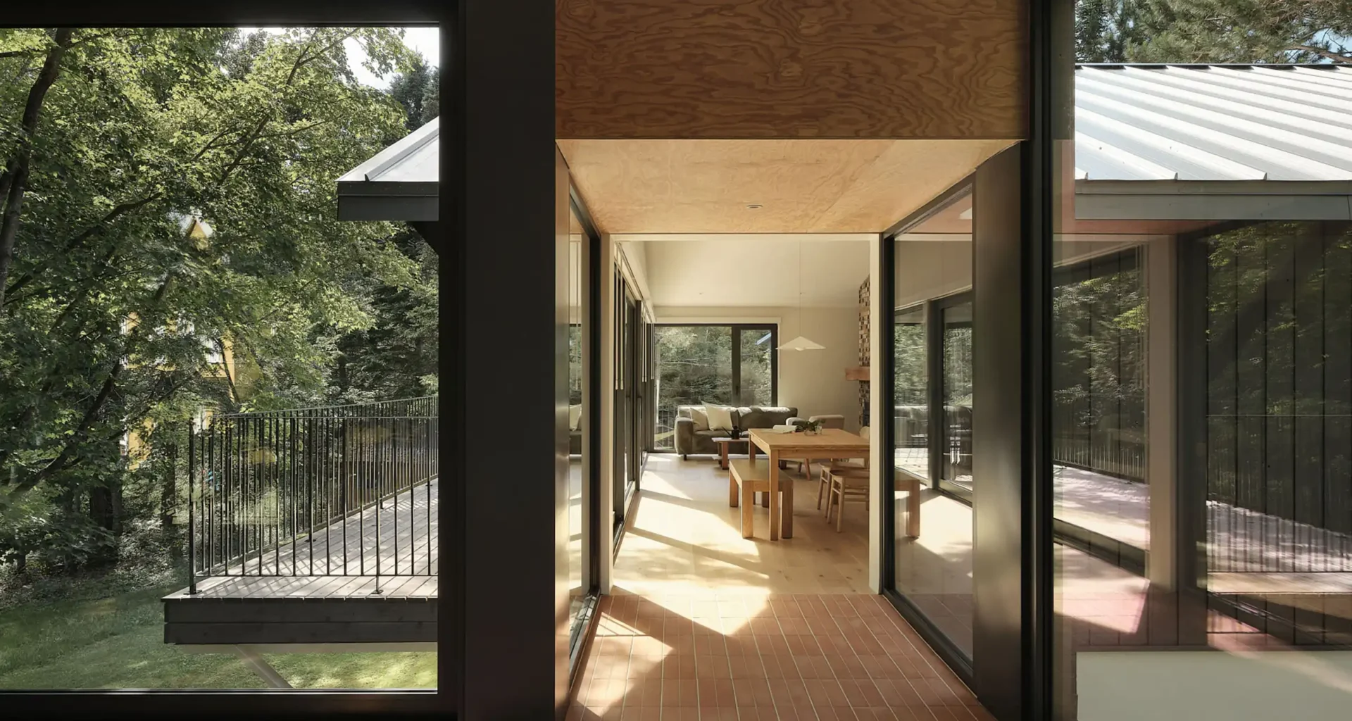 Interior view of the Saint-Ferréol Résidence showing an aerial walkway with terracotta flooring and glass walls connecting a modern timber pavilion to the original home.