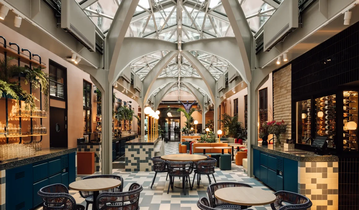 Interior of the Hobo Hotel Oslo social hub by Studio Aisslinger featuring a vaulted glass roof, checkered flooring, and lush greenery.