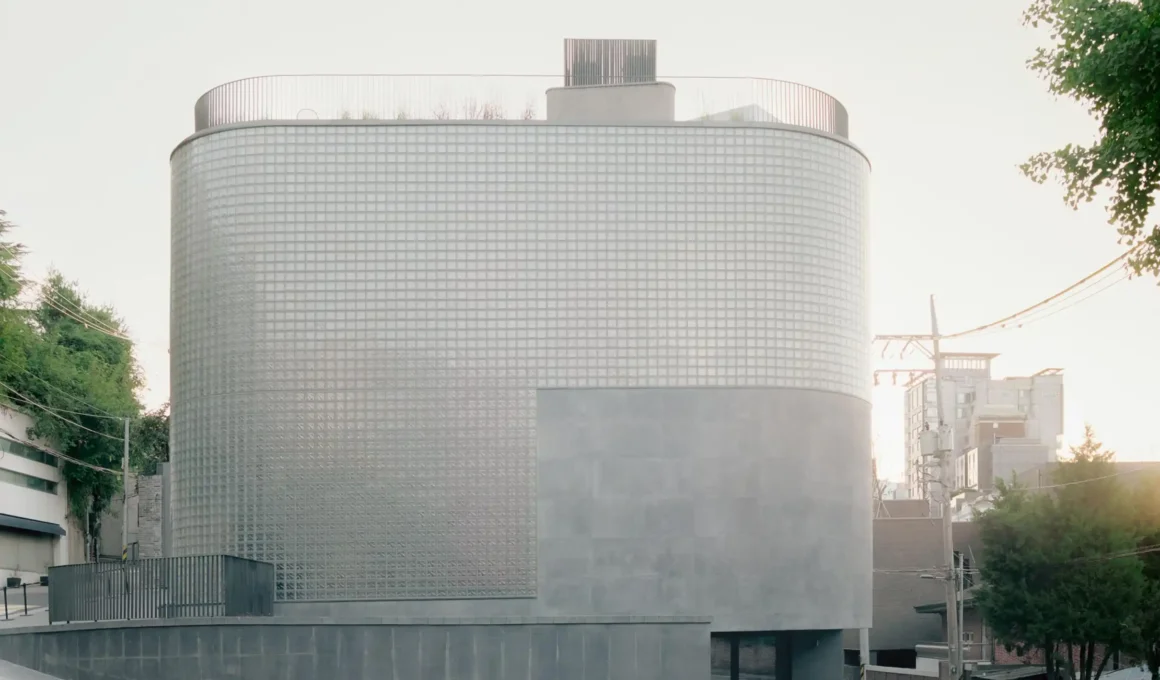 A monolithic three-story retail building in Seoul featuring a curved glass-block facade atop a textured grey concrete base, designed by Stocker Lee Architetti for Wooyoungmi.