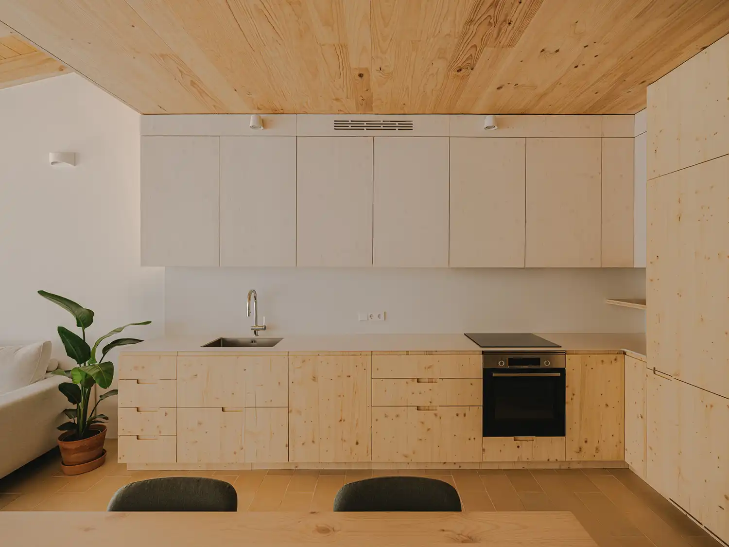 Close-up of the minimalist wooden kitchen in 130AUS with light-colored timber cabinetry, integrated appliances, and a seamless wood ceiling.
