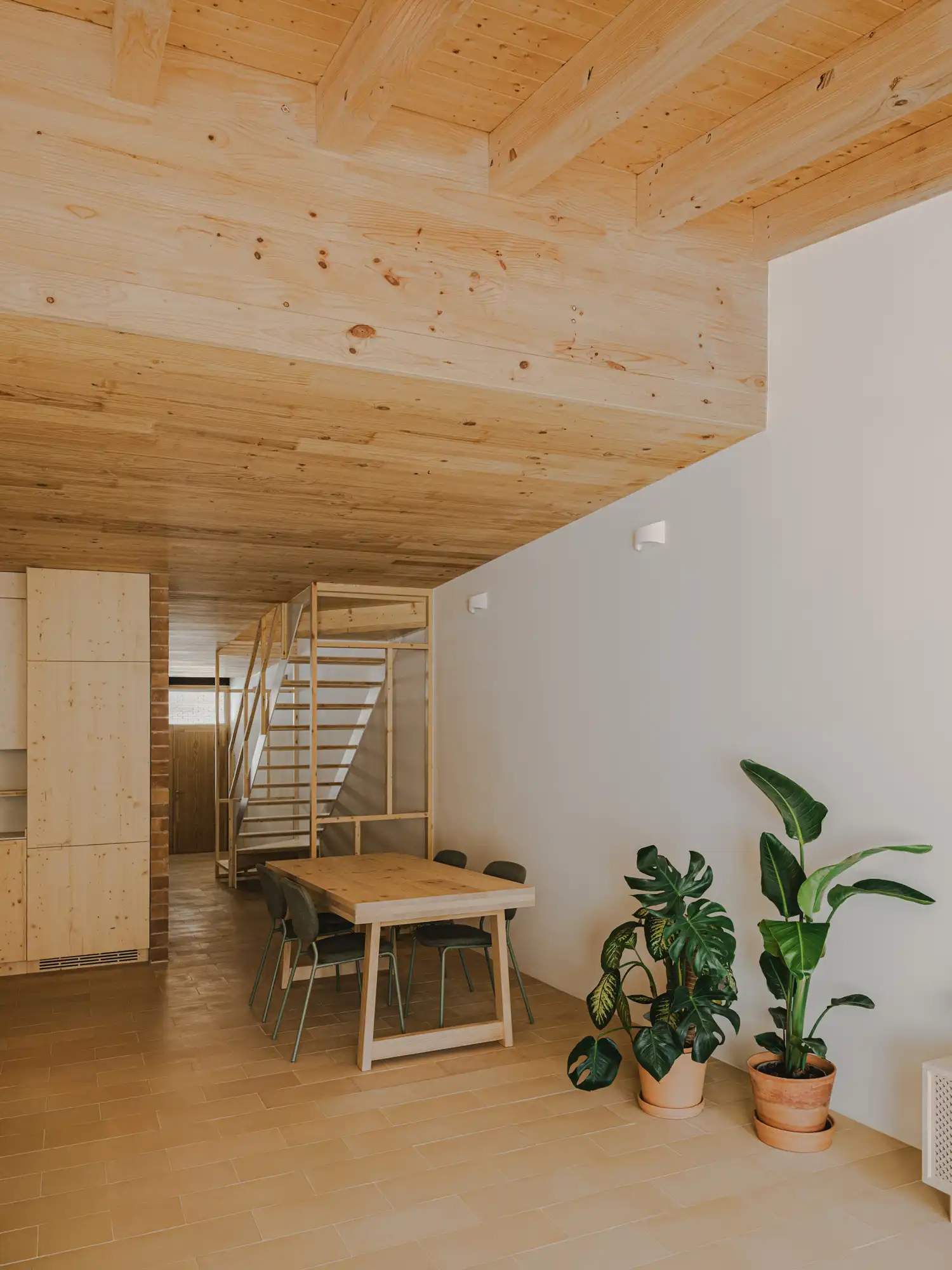 An open-frame wooden staircase in the center of 130AUS Sabadell, situated between a brick wall and the dining area.