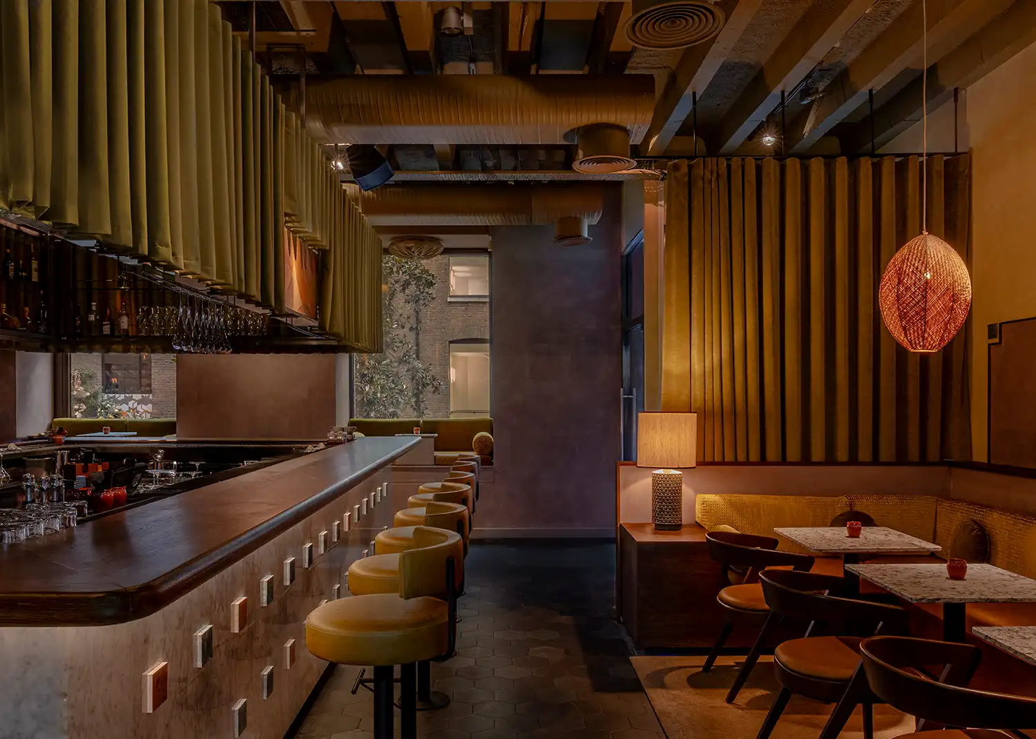 Perspective view of Anise bar showing the deep green velvet perimeter curtain and tarragon leather stools.