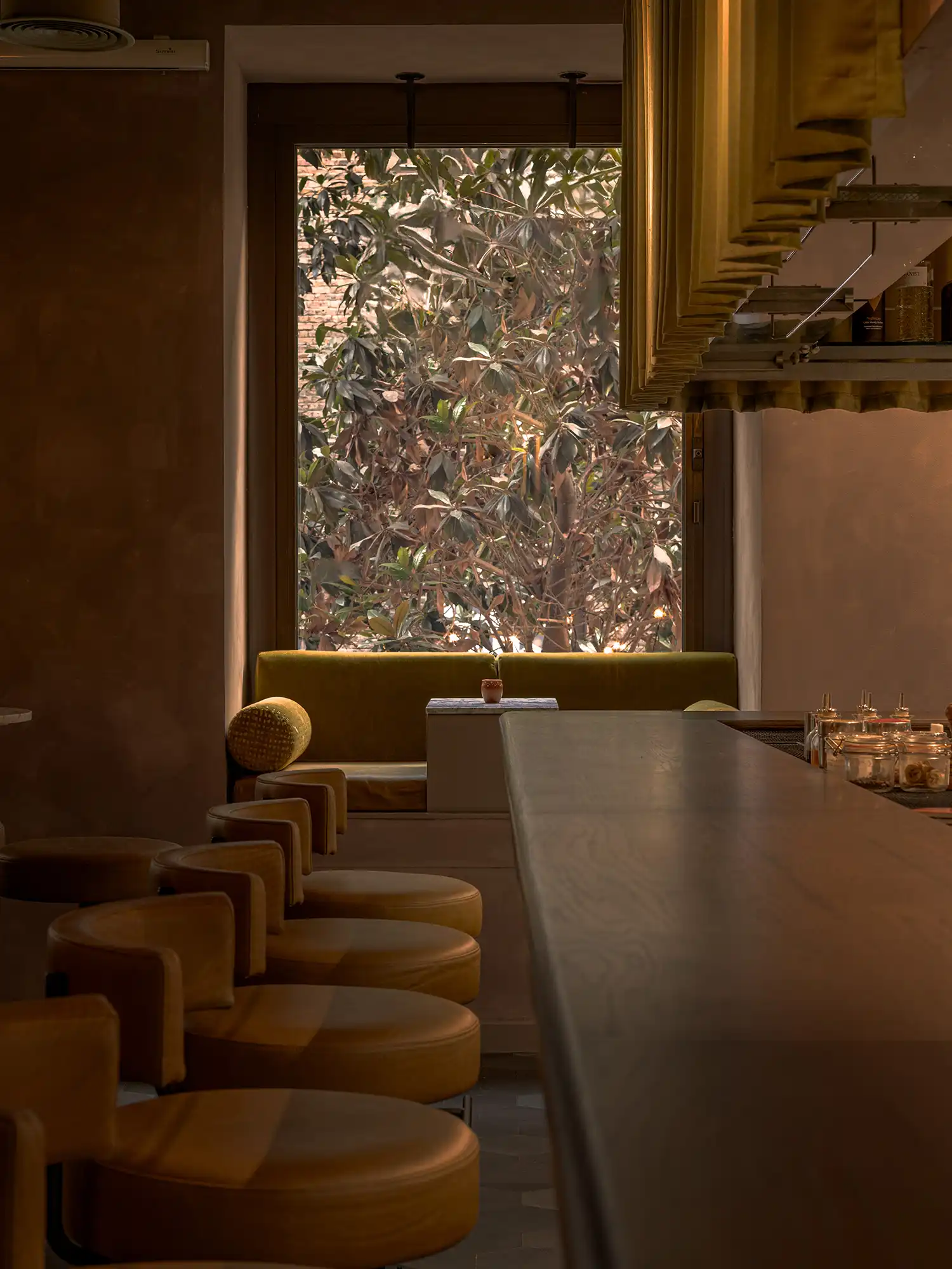 Wide view of the dark oak bar top looking toward an industrial window seat with greenery.