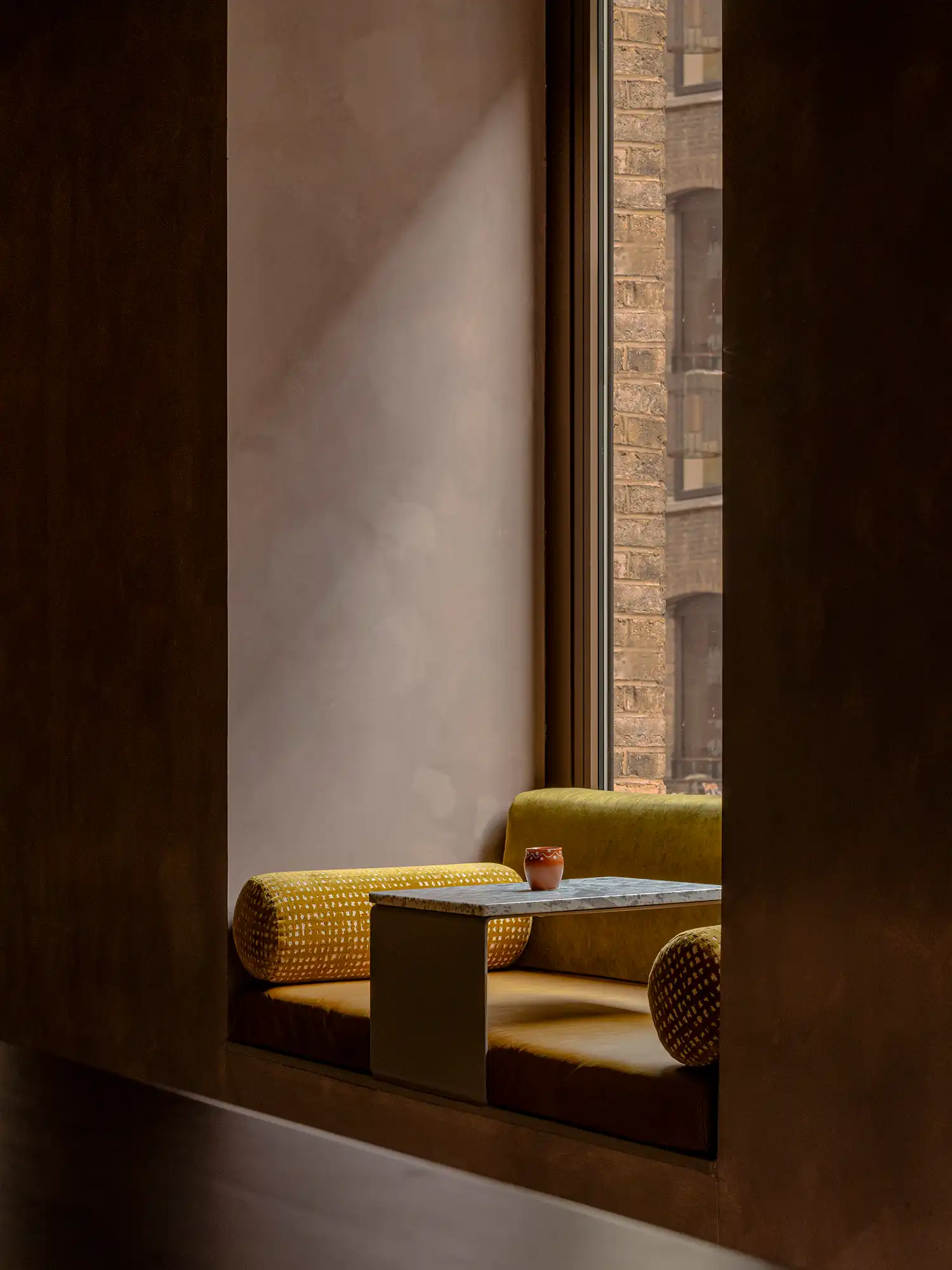 Close-up of a window seating nook with a marble table and green velvet cylindrical cushions.