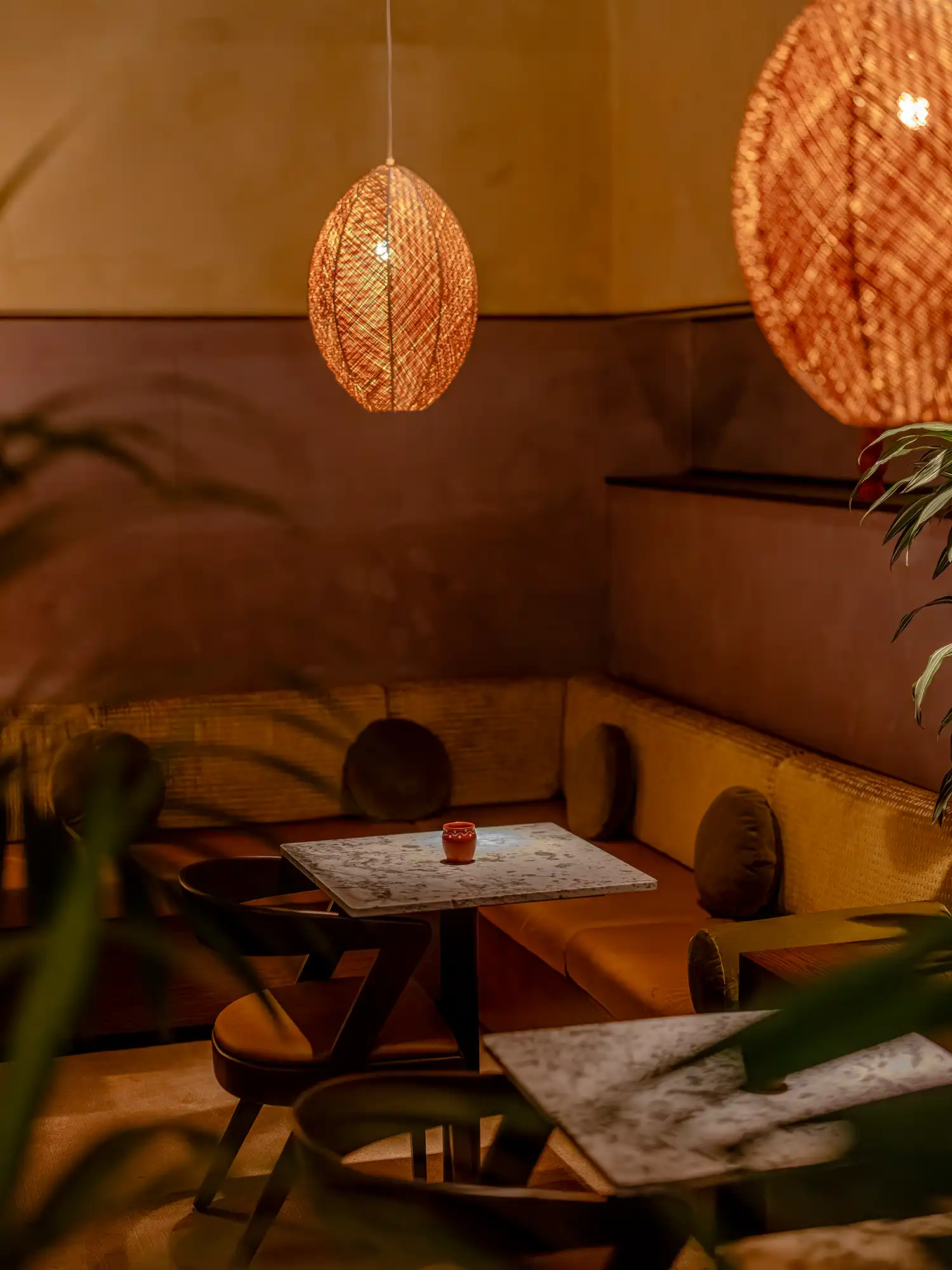 Detail of a lounge booth with Bauwerk limewash walls and a glowing rattan pendant lamp.