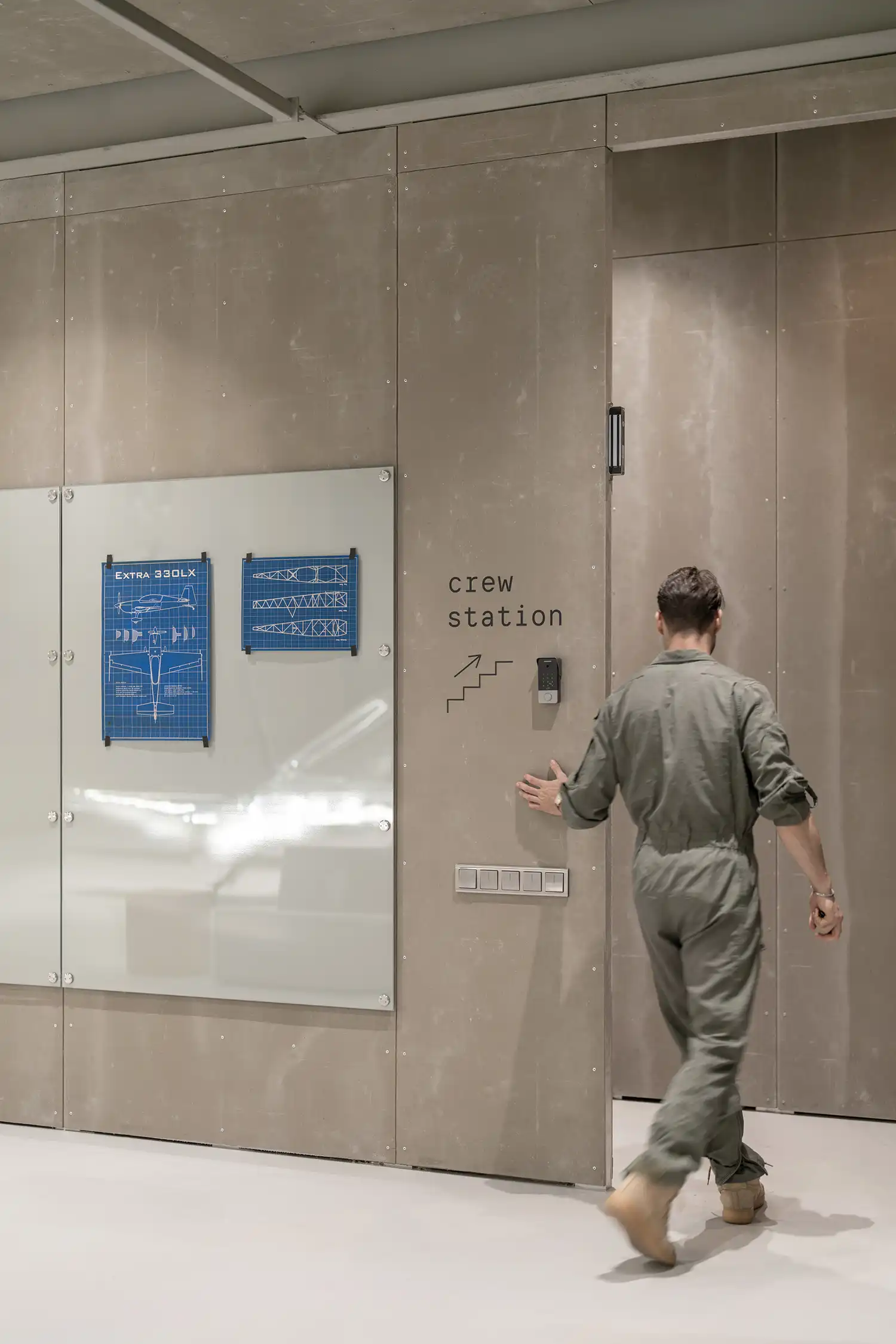 A man in a flight suit walking through a doorway labeled "crew station" next to integrated glass planning boards.