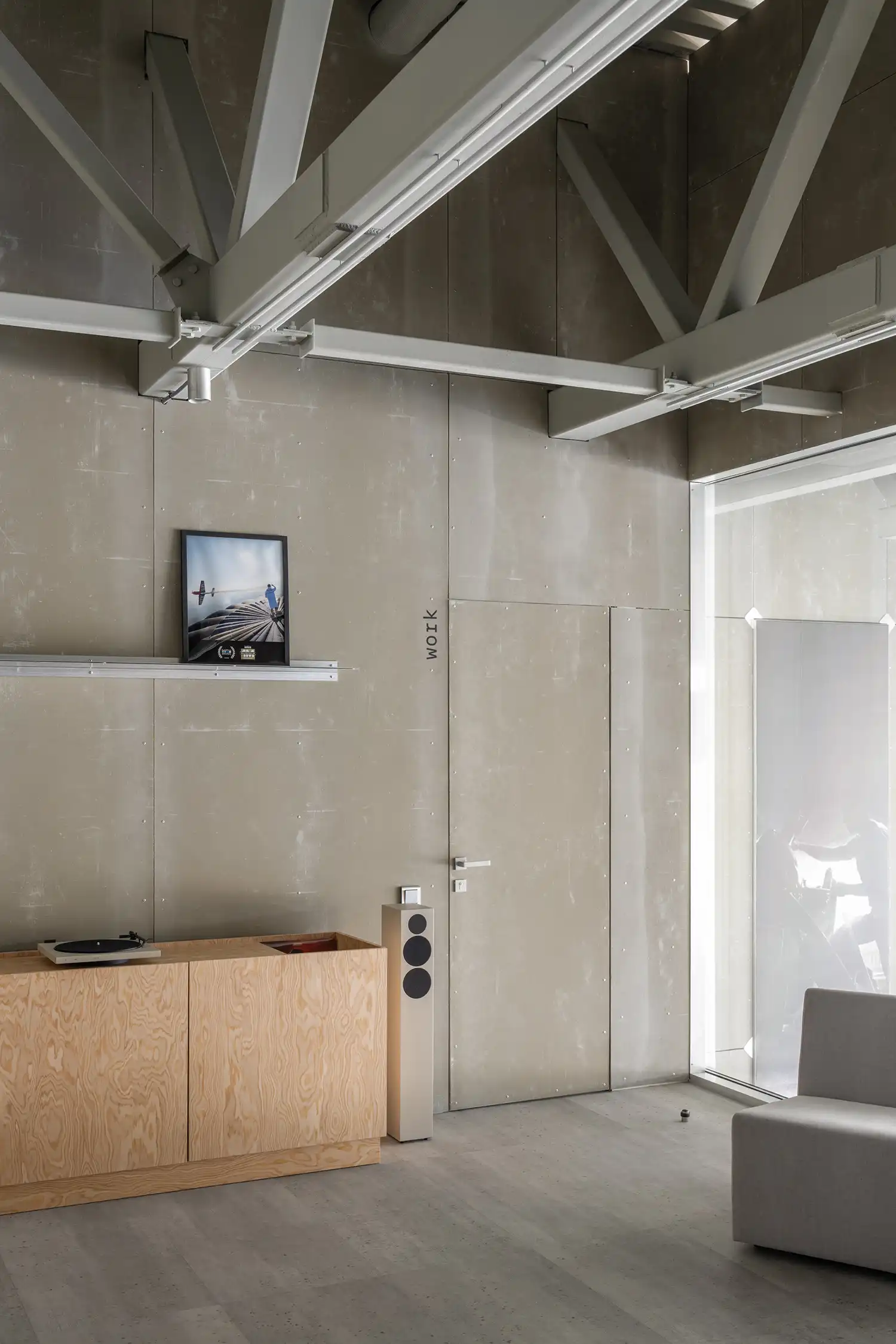Interior leisure area with a plywood cabinet, a modern grey sofa, and a large window overlooking the hangar.