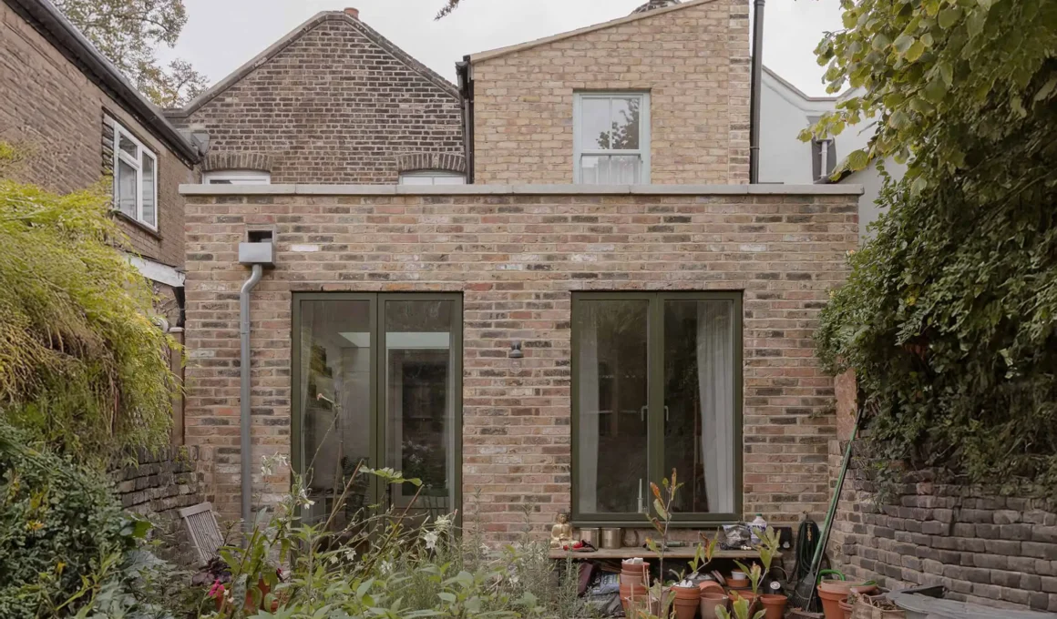 The new brick-clad rear extension of a Hackney mews house by Architecture for London, featuring triple-glazed green-framed doors.