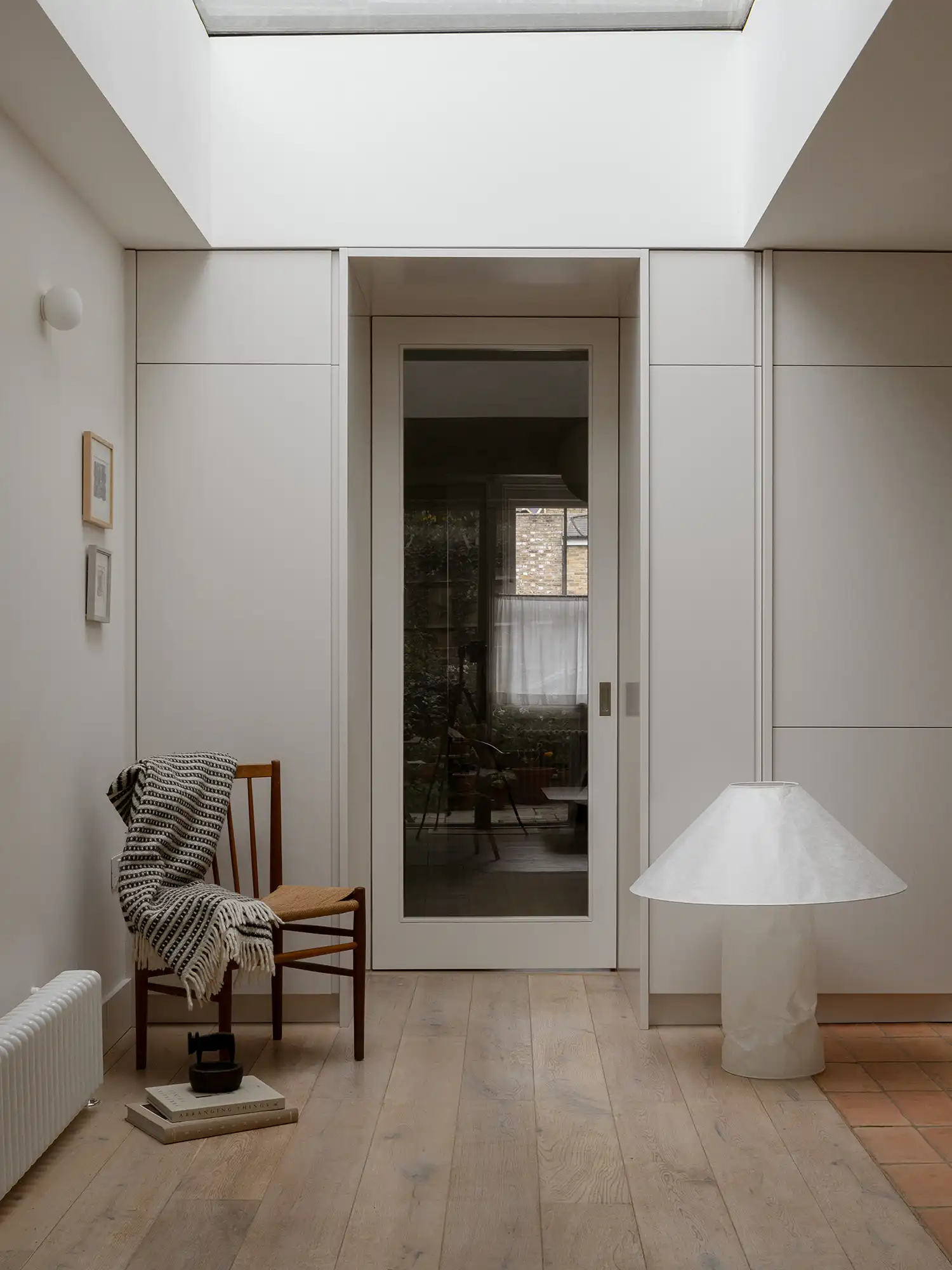 The architectural threshold where oak floorboards meet red clay tiles under a large skylight.