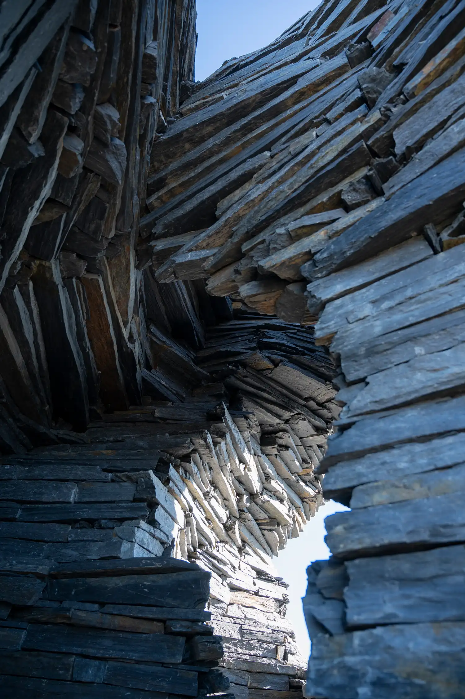 A group of people manually stacking thin black stone slabs to build a curved wall structure.