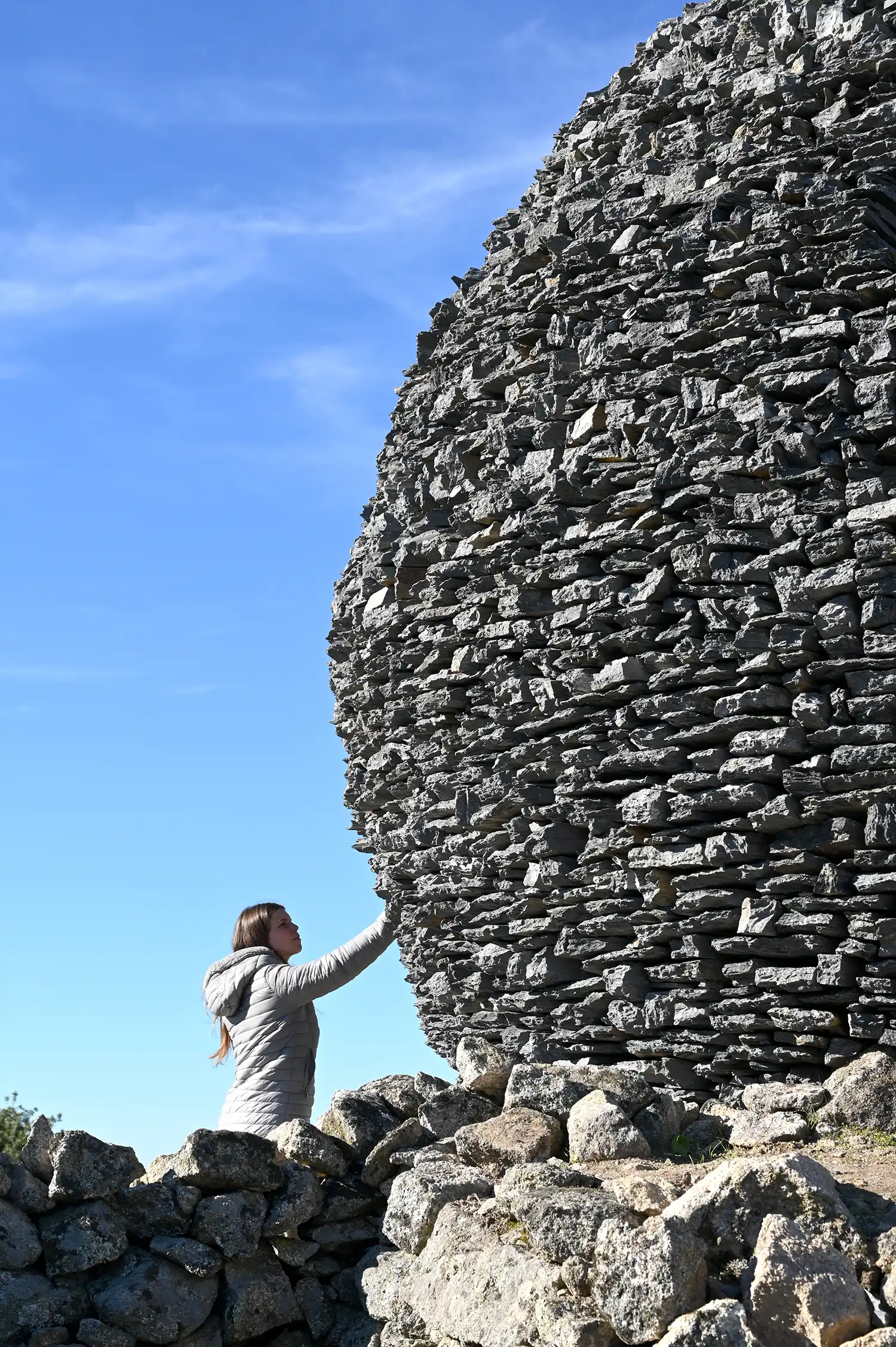 A group of people manually stacking thin black stone slabs around a curved framework.