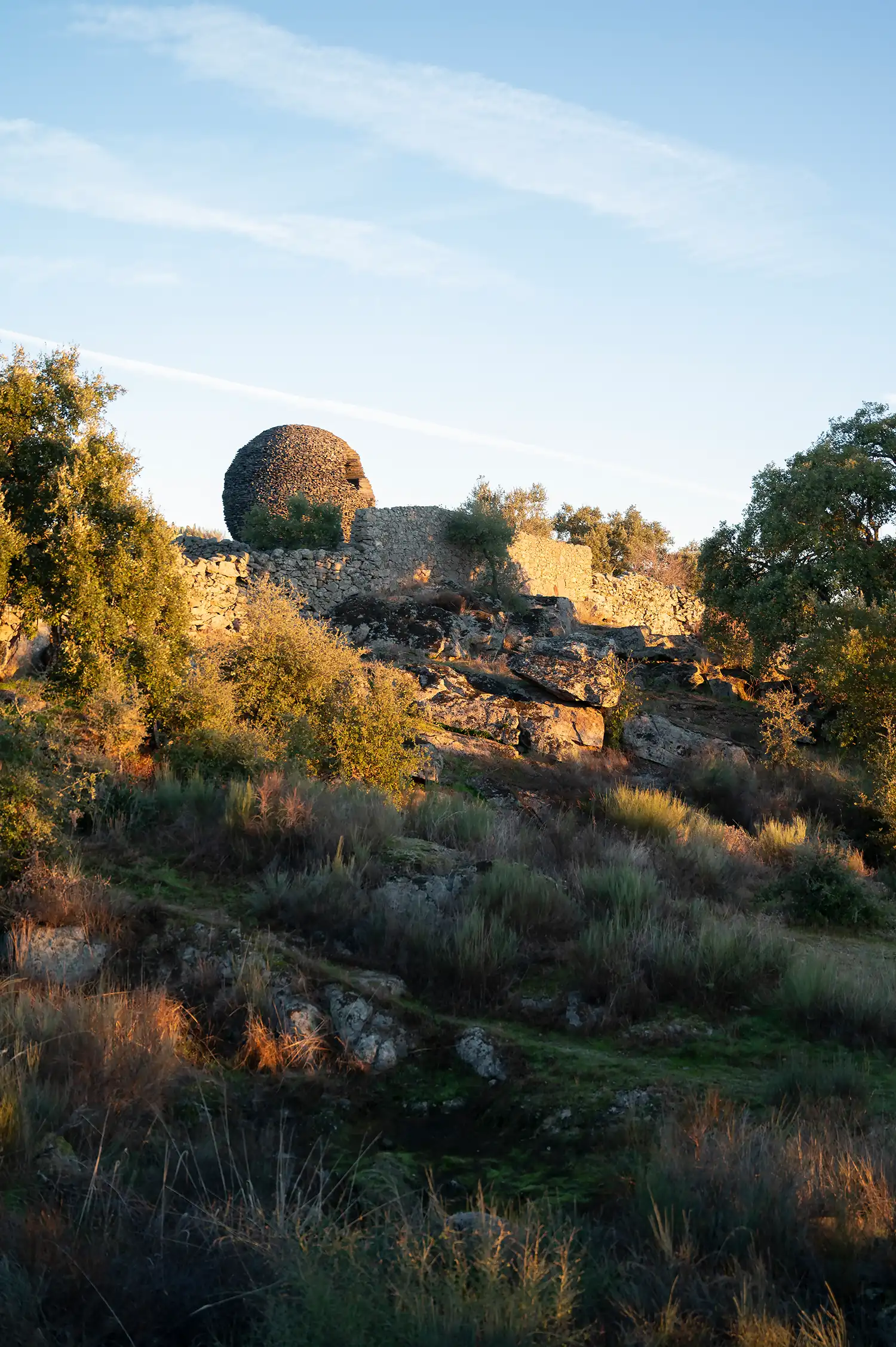 The stone sphere seen from a distance, integrated into the rocky terrain and wild vegetation.