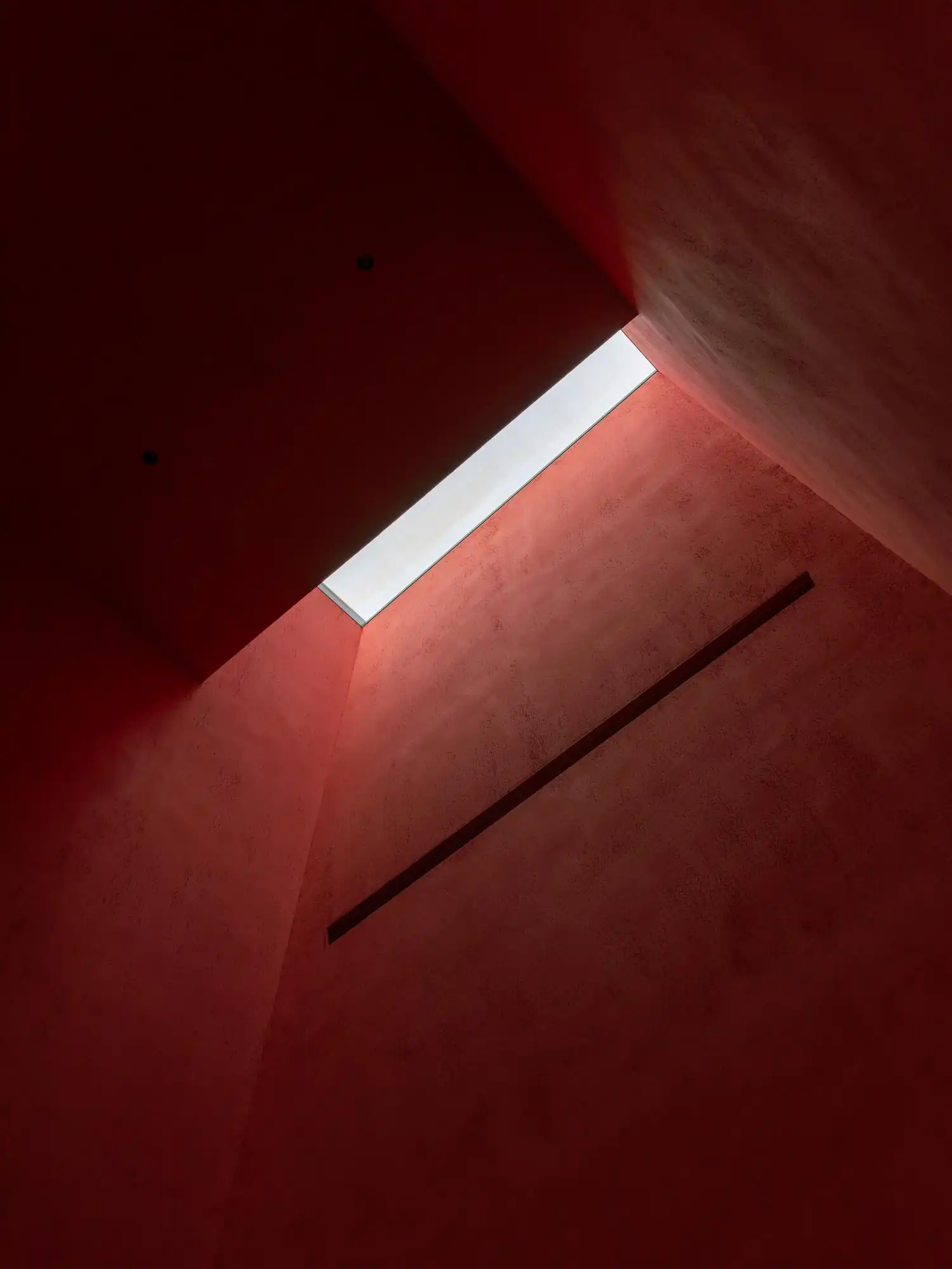 Interior view looking up a deep, rectangular lightwell with textured reddish-pink walls leading to a bright skylight.