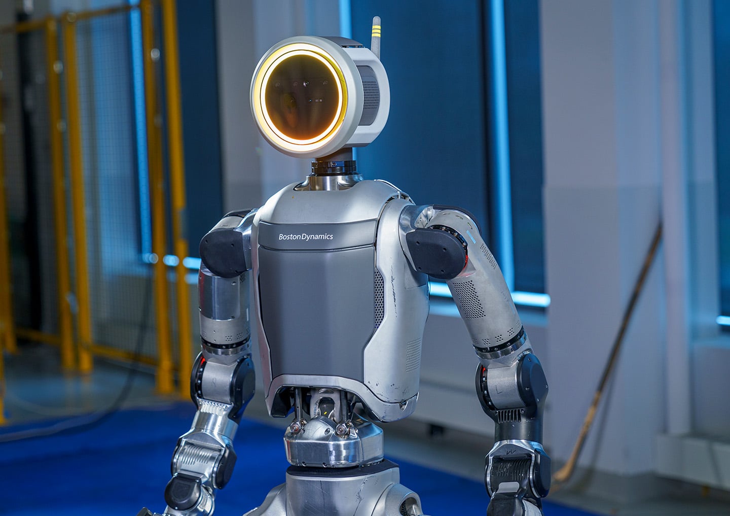 A close-up of the Atlas robot’s silver industrial torso and circular glowing head sensor, displaying the Boston Dynamics branding.