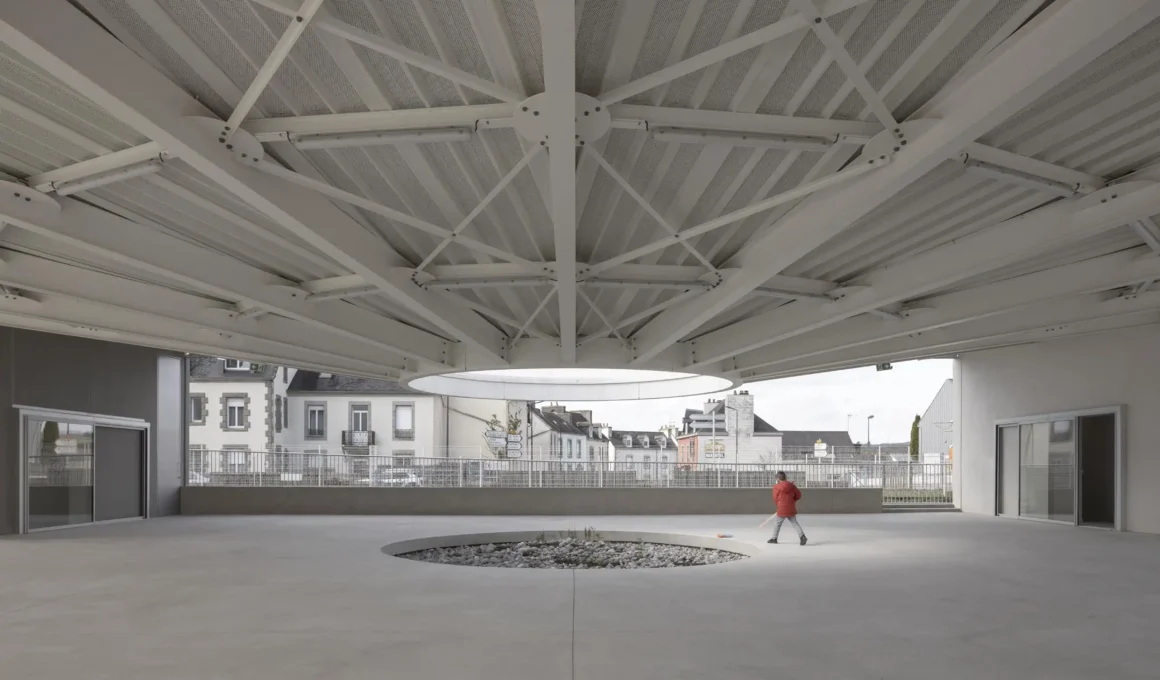 Interior view of a circular hall with a radiating white steel roof structure and a central circular opening.