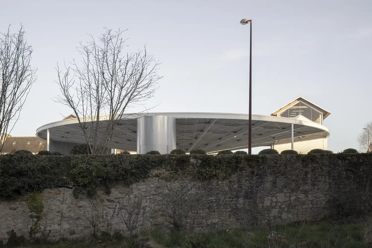 Low-angle exterior view of a flat circular roof appearing to float behind an old stone retaining wall.