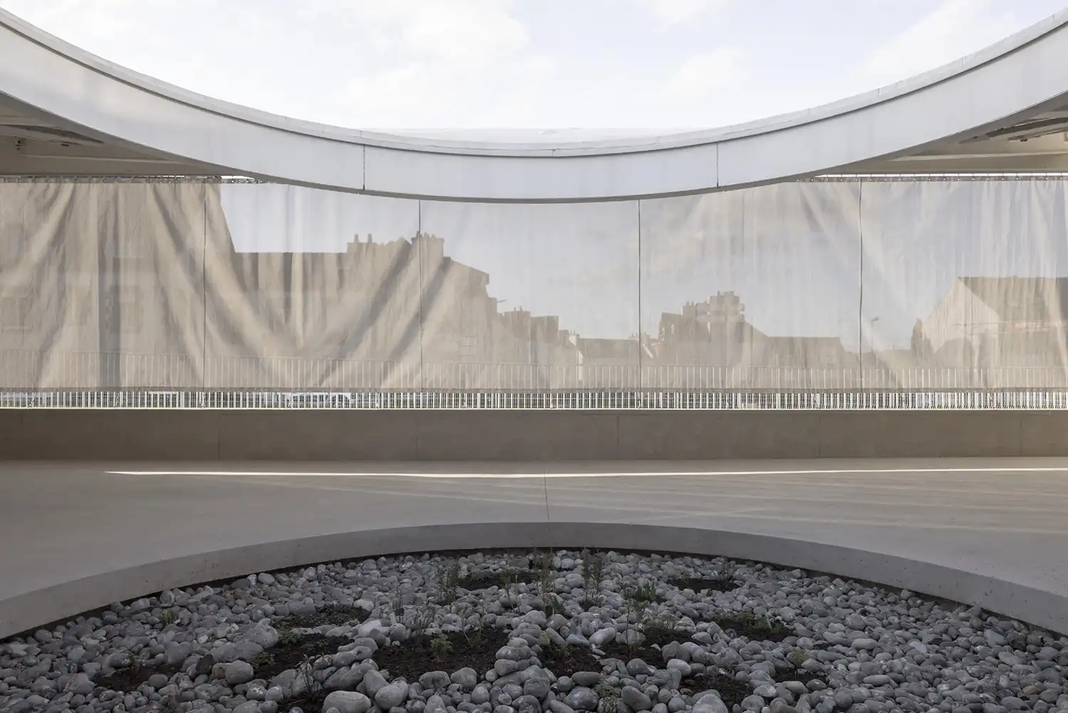 Close-up of a micro-perforated translucent curtain hanging in a curve over a stone-filled central patio.