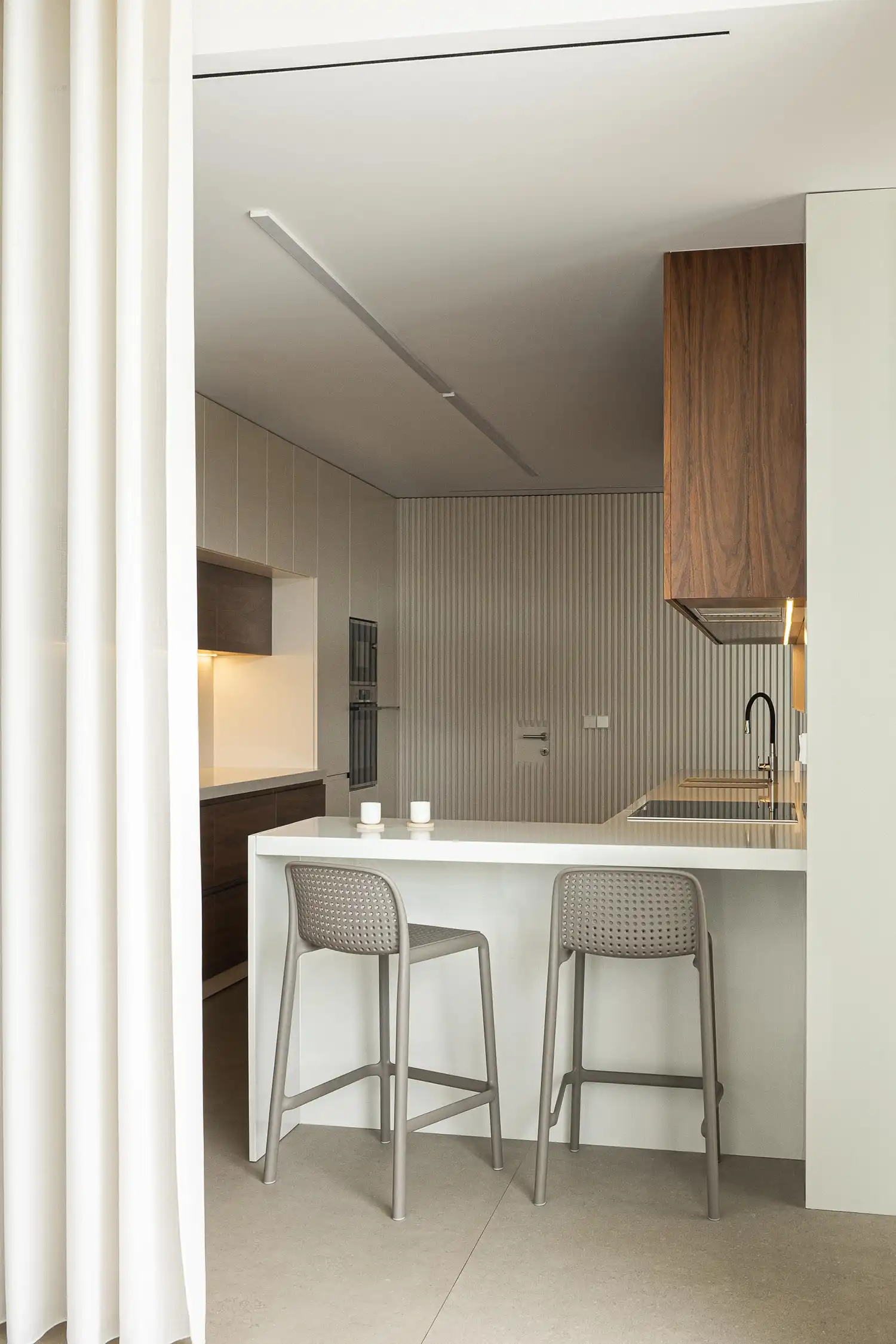 Modern minimalist white kitchen with a wooden breakfast bar and sleek stools.