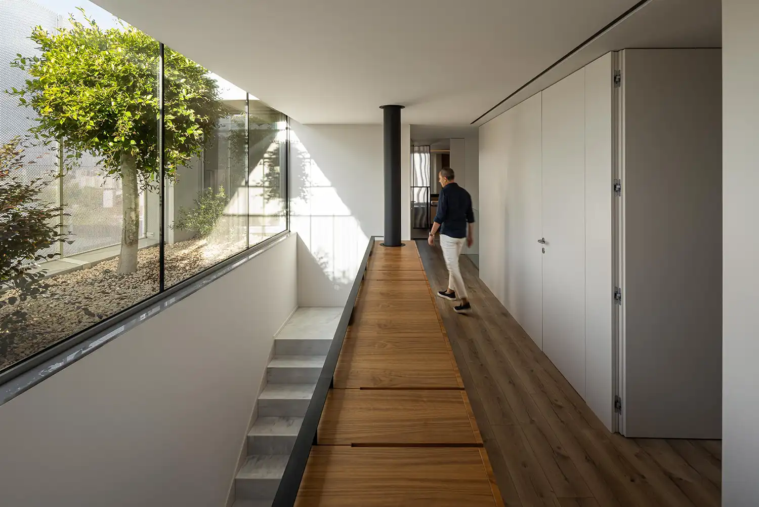 Upper floor circulation area with wooden flooring and a view of an internal courtyard garden.