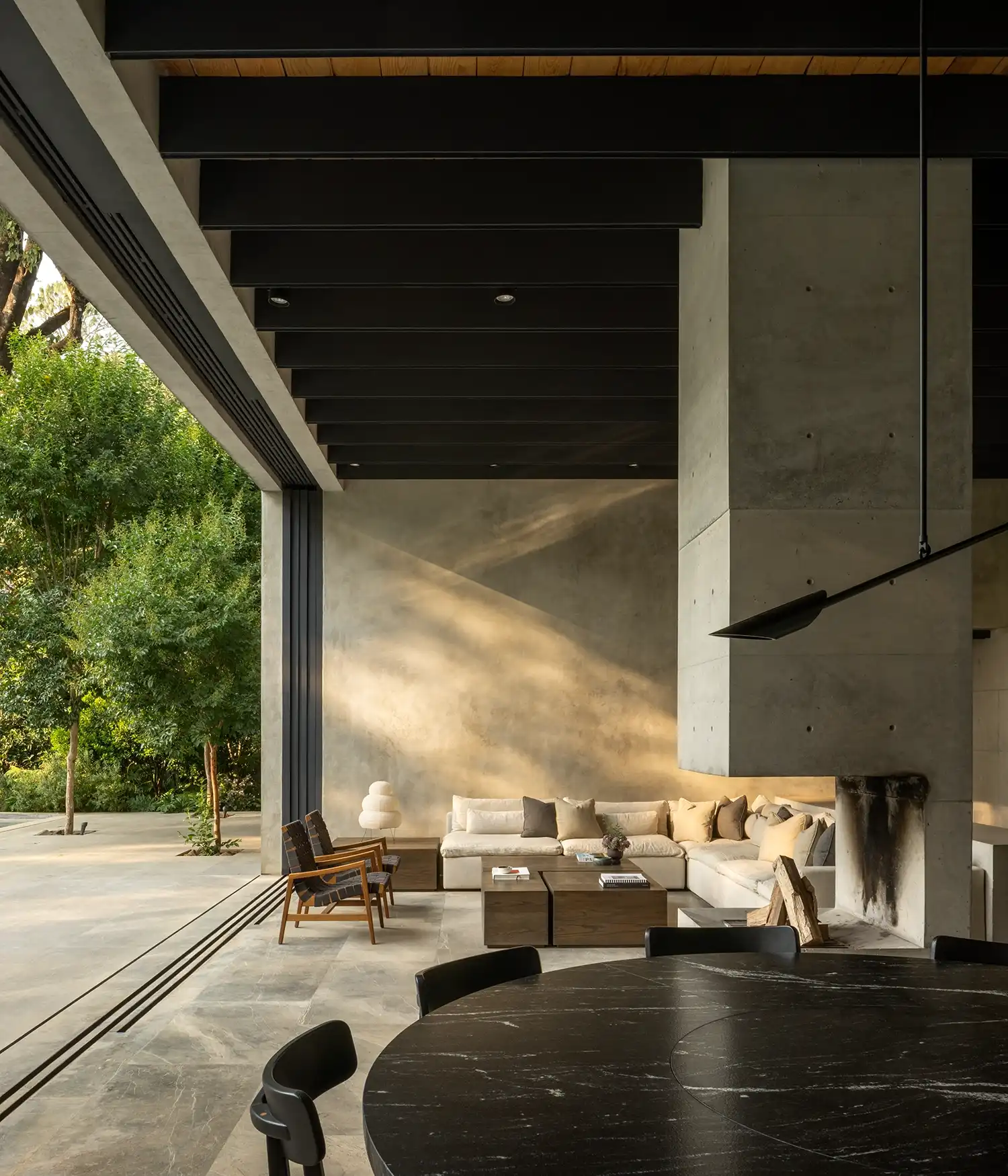 Modern living area with a large concrete fireplace and sliding glass doors opening to a forest.
