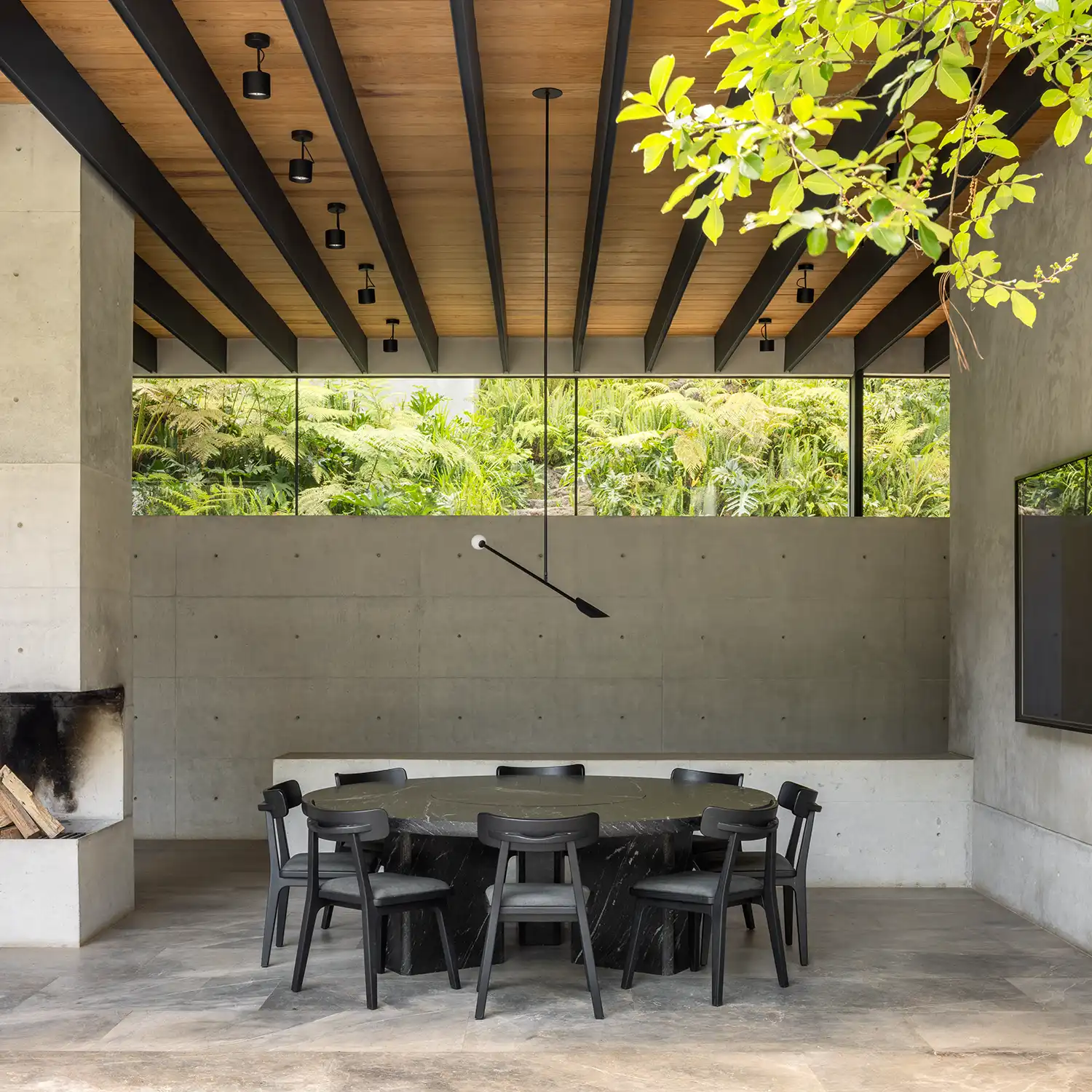 A circular black marble dining table under a wood-slatted ceiling with steel beams.