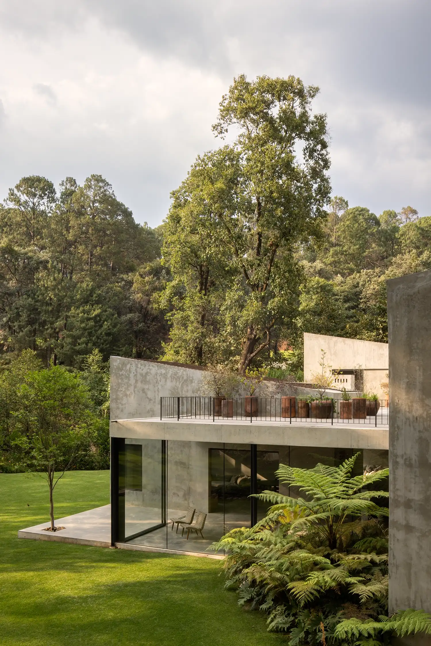 Exterior view of Casa en Avándaro showing the concrete base and glass facade amidst ferns.