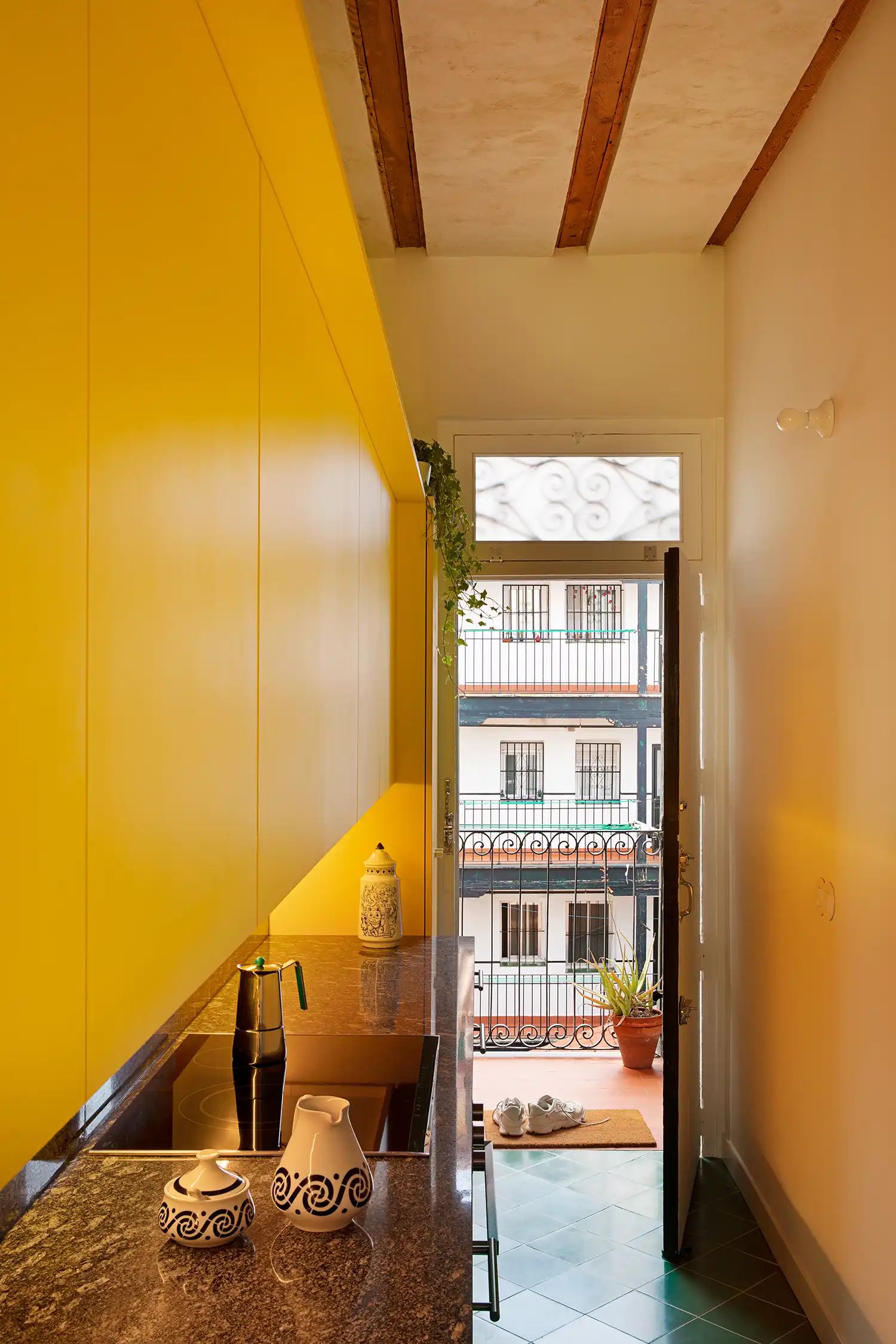 Narrow modern kitchen with yellow cabinets leading to a traditional Spanish balcony in Lavapiés.