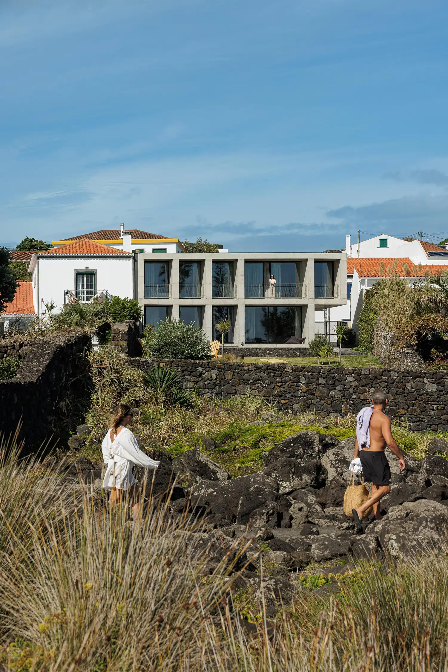 Wide shot of the concrete house integrated into the rocky Azorean landscape with people walking in the foreground.