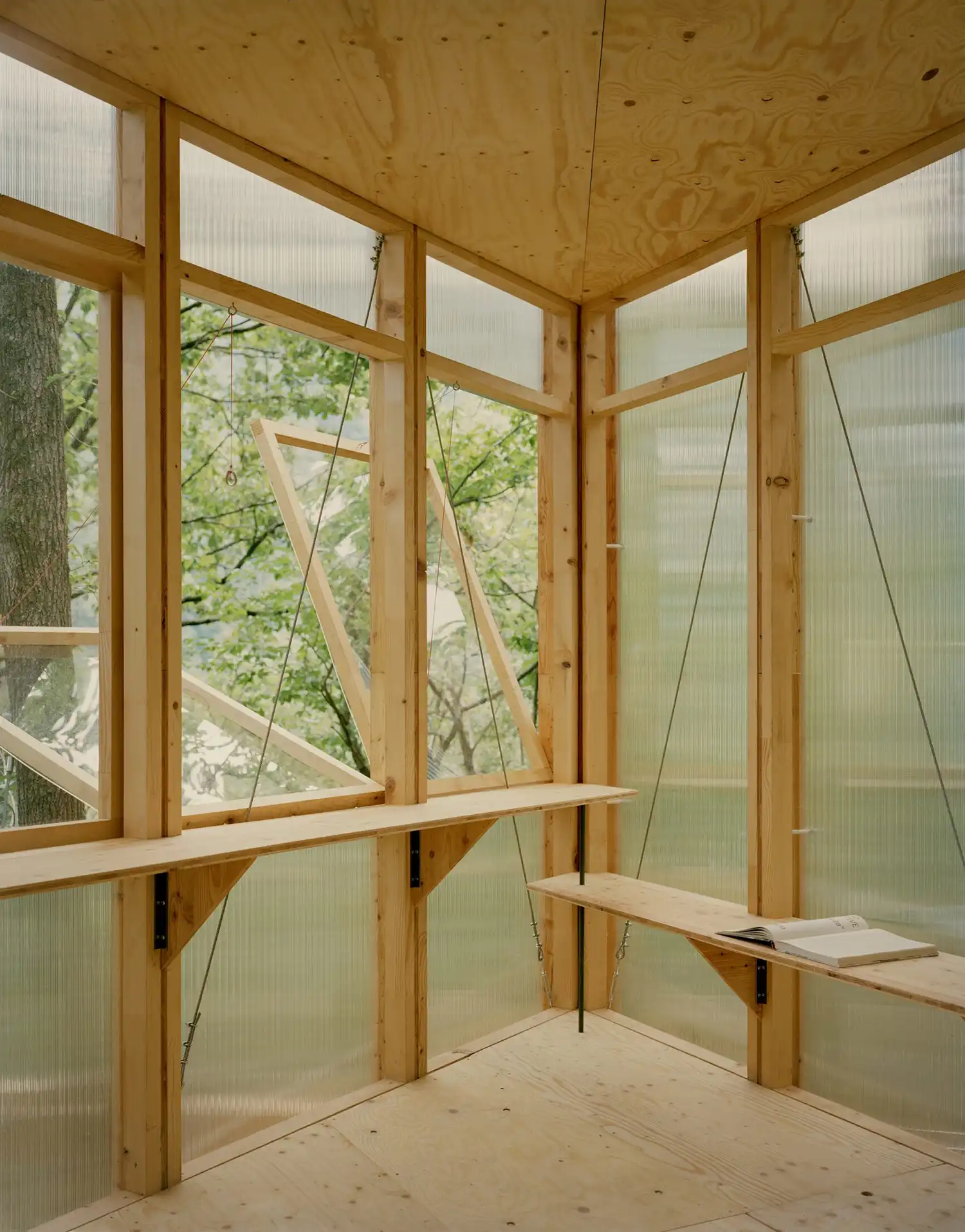 Interior perspective of the cabin's corner with openable window flaps and a wooden bench integrated into the spruce timber frame.