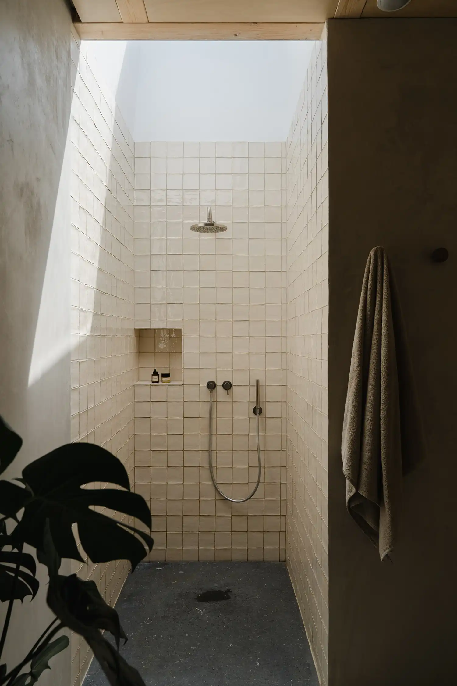 Minimalist walk-in shower with cream-colored square tiles and a large skylight overhead.