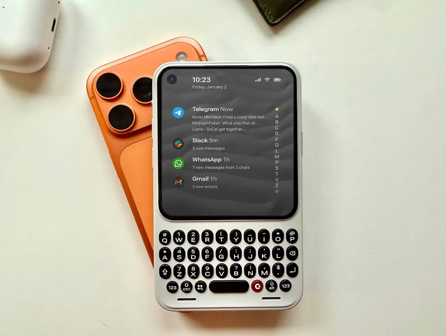 Clicks Communicator white QWERTY phone next to an orange smartphone.