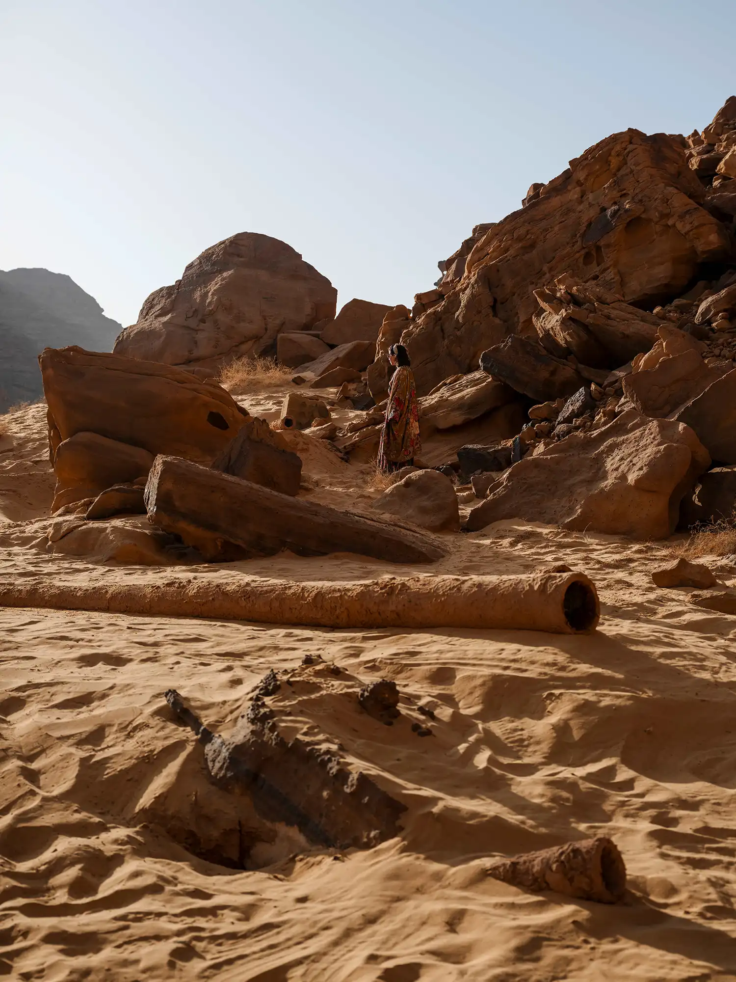 Tarek Atoui’s sound installation featuring horizontal tube-like forms on the sand, surrounded by jagged rock formations.