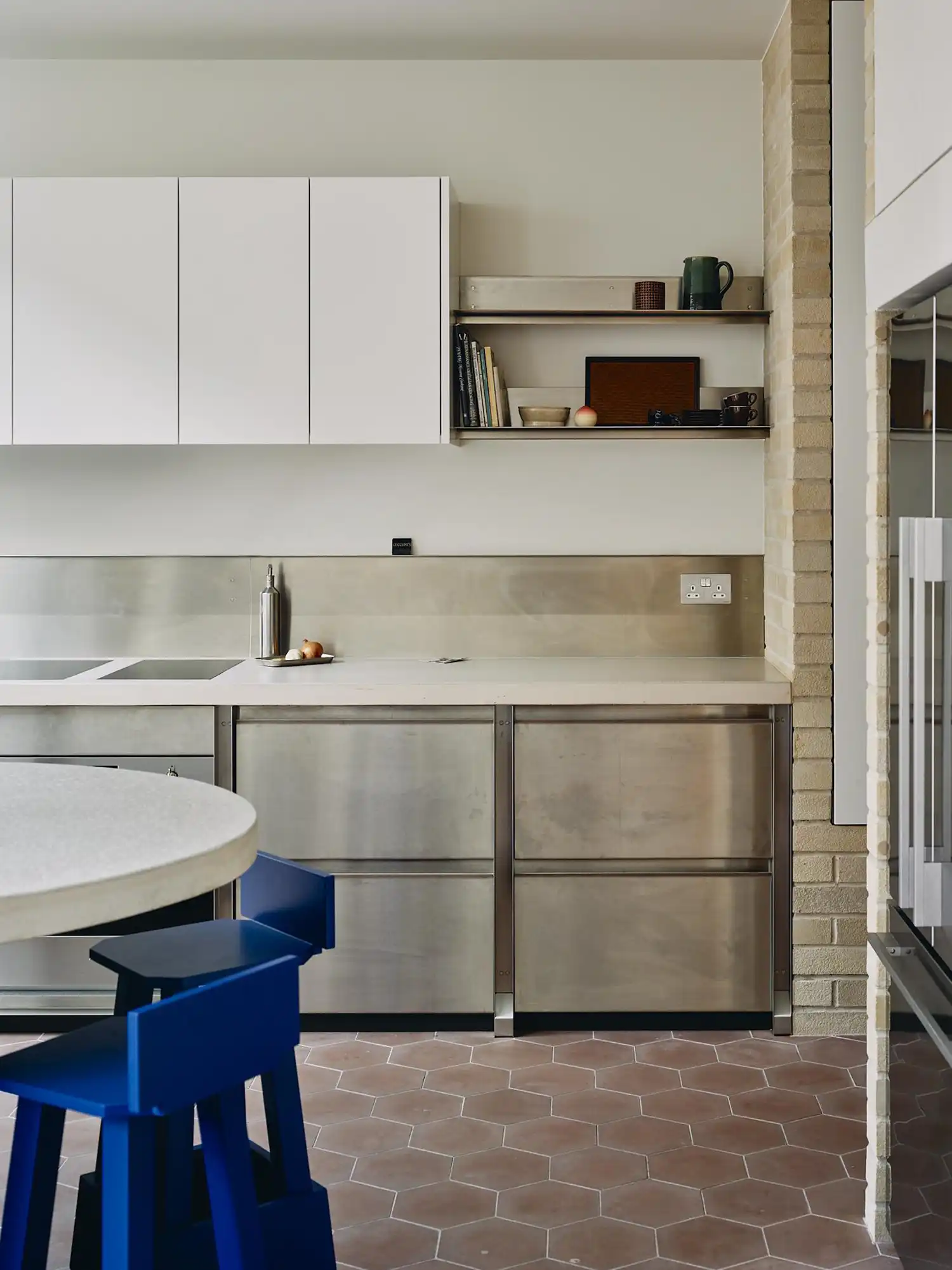 Modern kitchen with stainless steel cabinets, concrete worktops, and bright Yves Klein blue bar stools.