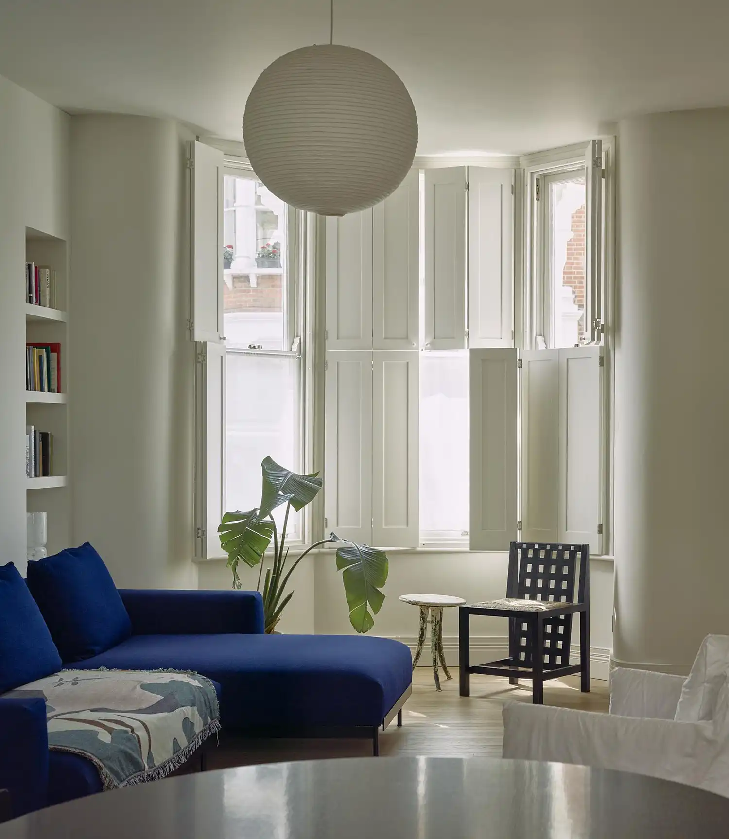 Living room with a deep blue velvet sofa, a paper lantern pendant, and white window shutters.
