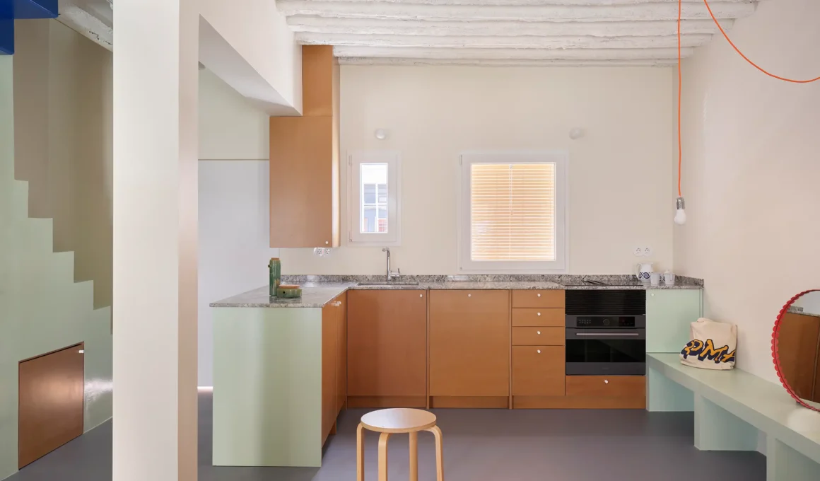 Minimalist kitchen in Madrid’s TET House featuring wood cabinetry, mint green accents, and exposed white ceiling beams.