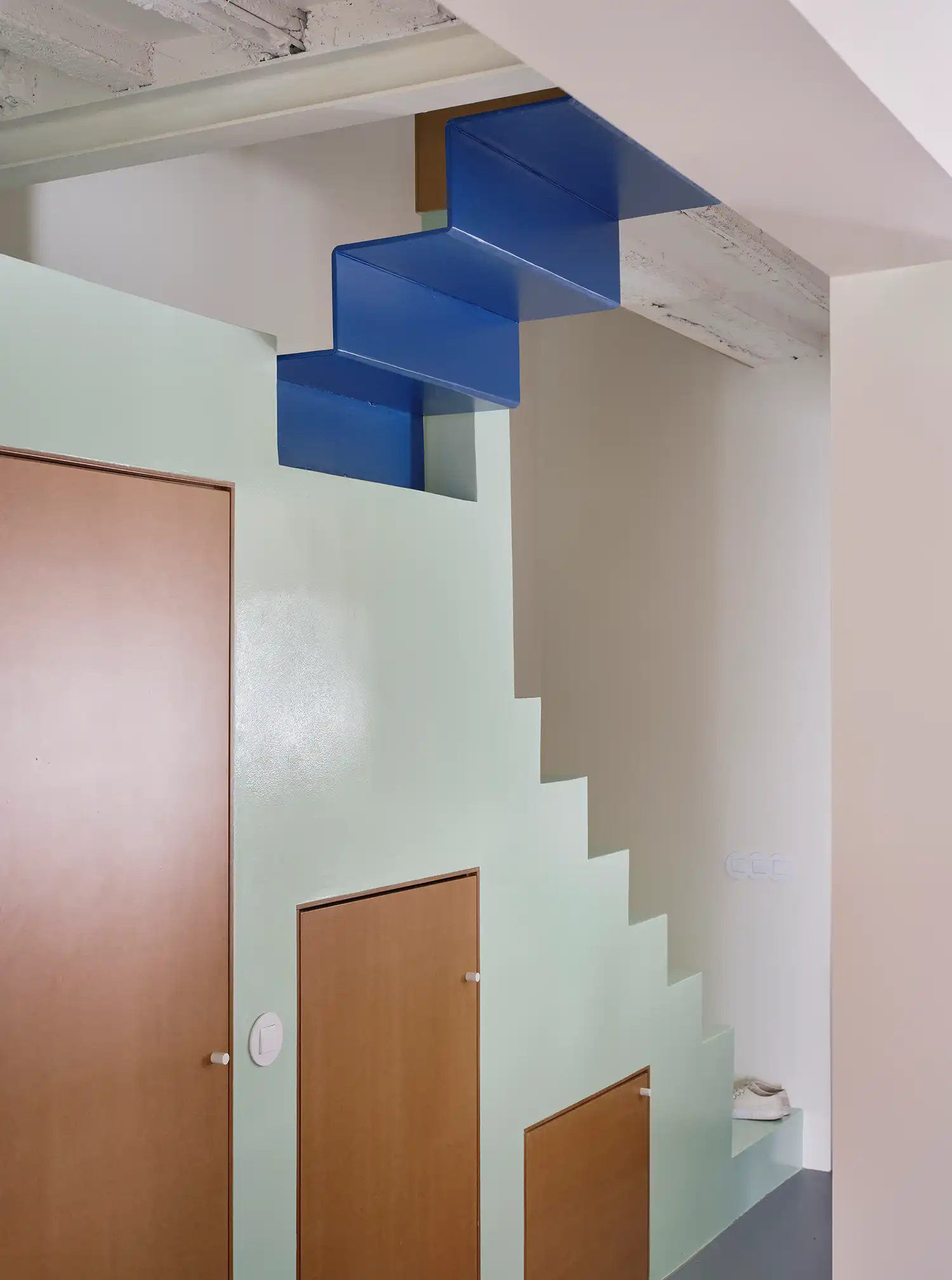 Close-up of a sculptural blue metal staircase integrated into a pale green wall within a modern renovation.