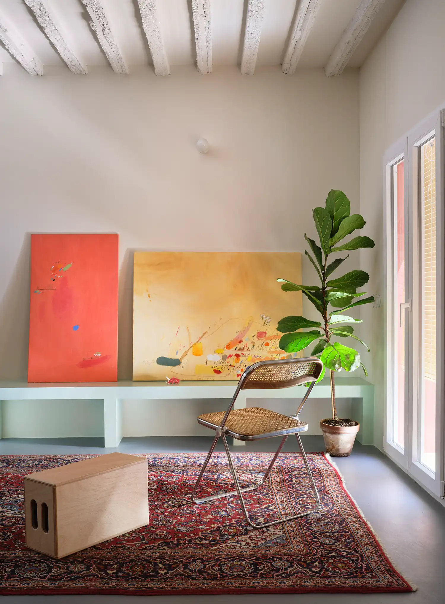 Bright living room with white walls, large abstract paintings, a vintage folding chair, and a Persian-style rug.
