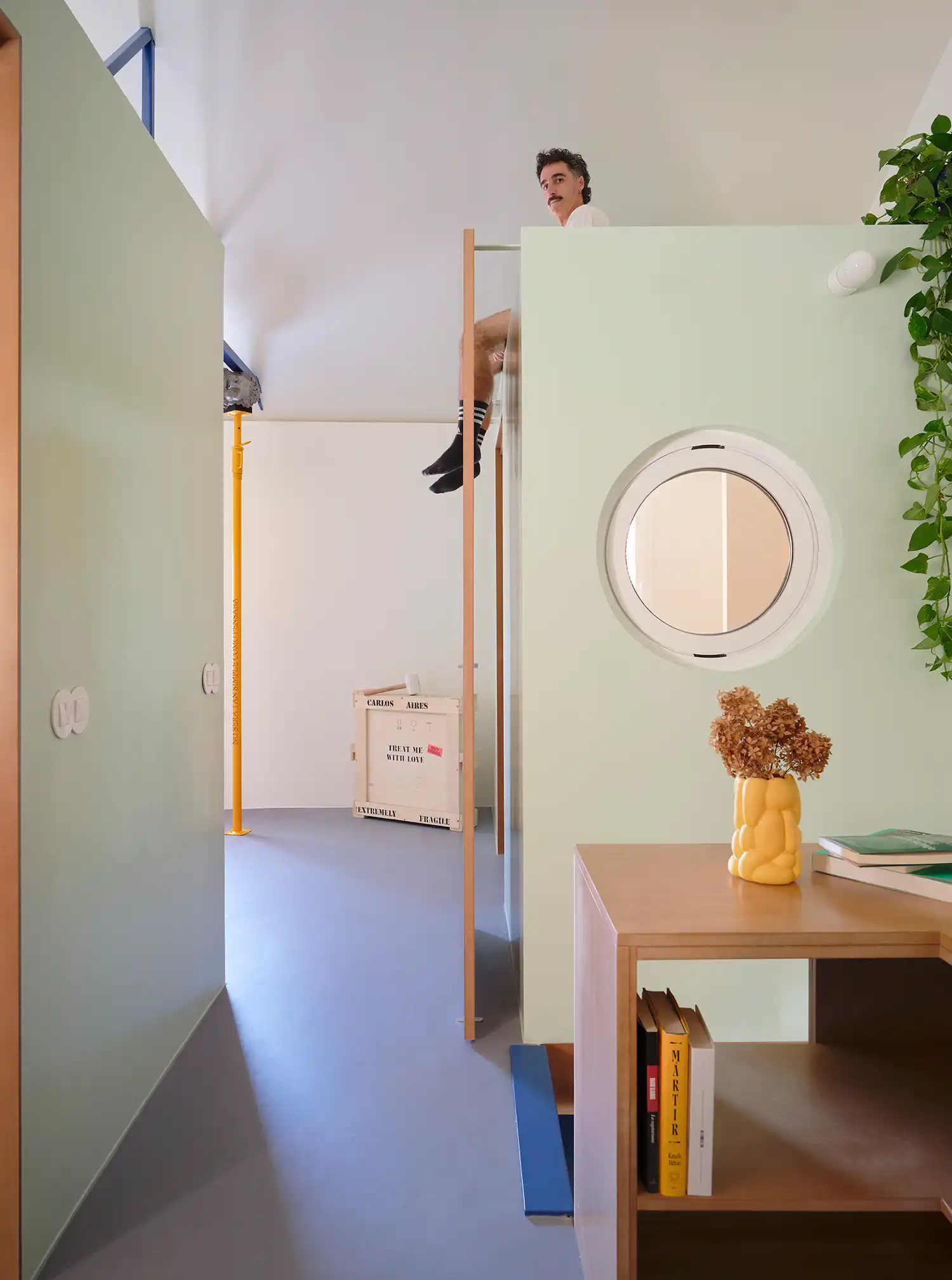 Interior view of TET House showing pale green partitions, a circular window, and a glimpse of the upper mezzanine level.