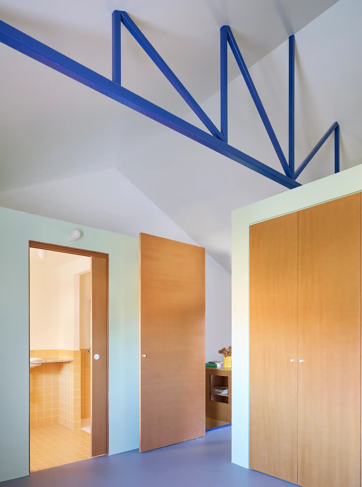 Modern bedroom and bathroom modules in a Madrid renovation featuring blue steel trusses and wooden doors.